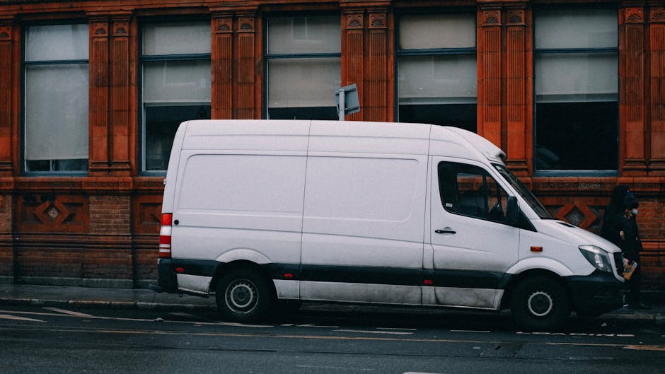A front view of a vintage Volkswagen van painted in light blue with a white top, parked on a cobbled street. The vehicle features round headlights, rectangular indicators, and a distinctive front gril