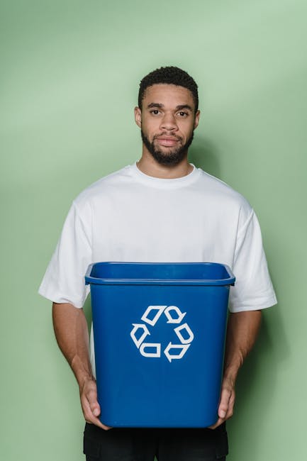 A cream-colored cotton drawstring bag placed on a white marble surface, alongside a black smartphone displaying a green recycling symbol on its screen. The bag appears to be used for packing or storin